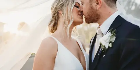 A bride and groom sharing a close moment, with the bride wearing a white dress and veil and the groom in a dark suit with a white boutonniere.