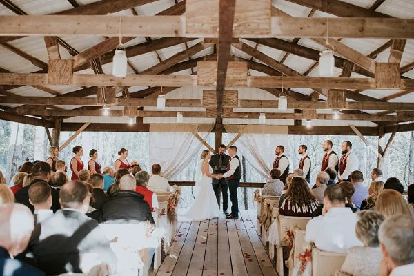 A wedding ceremony in progress inside a rustic wooden pavilion with exposed beams and a wooden floor.