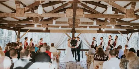 A wedding ceremony in progress inside a rustic wooden pavilion with exposed beams and a wooden floor.