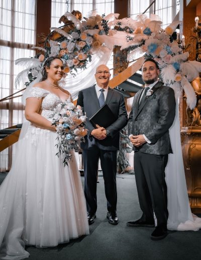 A wedding officiant stands between a bride and groom during a ceremony in a church setting.