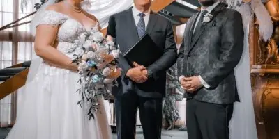 A wedding officiant stands between a bride and groom during a ceremony in a church setting.