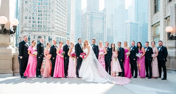 A wedding party consisting of a bride, groom, and attendants posing for a group photo in an urban setting.