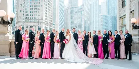 A wedding party consisting of a bride, groom, and attendants posing for a group photo in an urban setting.