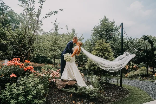 A bride and groom sharing a kiss in a garden setting with a lake visible in the background.