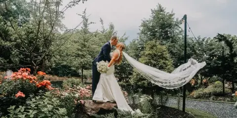A bride and groom sharing a kiss in a garden setting with a lake visible in the background.