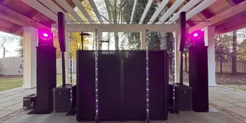 Professional DJ booth setup with speakers, lighting, and a DJ console at an outdoor venue.