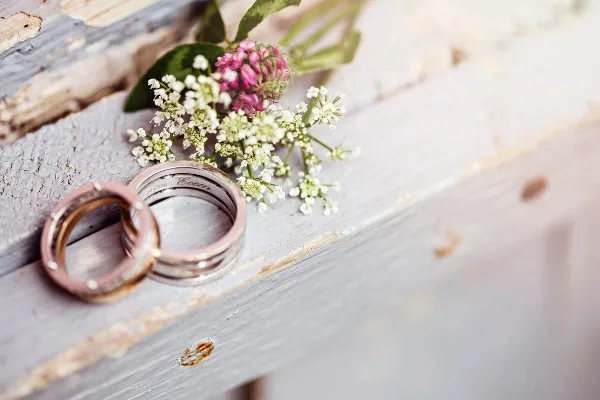 A pair of wedding rings resting on a rustic wooden surface next to a small bouquet of wildflowers.