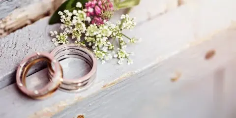 A pair of wedding rings resting on a rustic wooden surface next to a small bouquet of wildflowers.