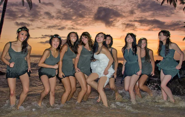 A bride and her bridesmaids posing together in the ocean at sunset.