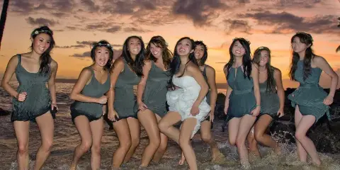 A bride and her bridesmaids posing together in the ocean at sunset.