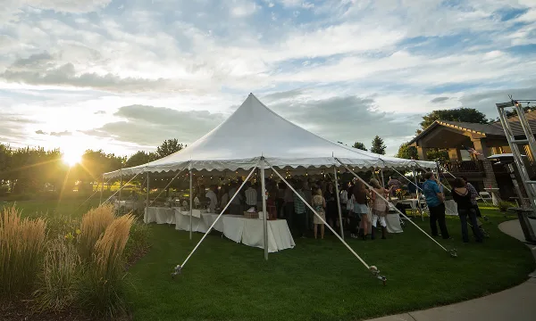 A large white event tent set up on a grassy lawn with tables and guests inside during the evening.
