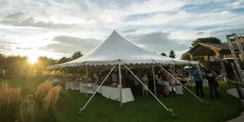 A large white event tent set up on a grassy lawn with tables and guests inside during the evening.