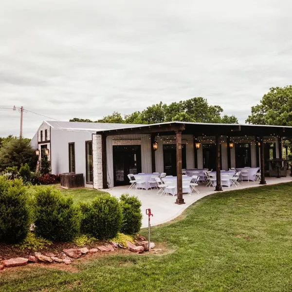 Exterior view of a white venue building with a covered patio featuring set-up tables and chairs.