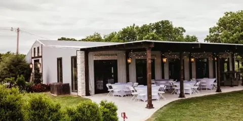 Exterior view of a white venue building with a covered patio featuring set-up tables and chairs.