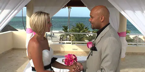 A bride and groom holding hands during a wedding ceremony at a beachside venue.