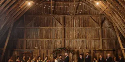 Interior of a wooden barn venue with string lights and a wedding ceremony in progress.