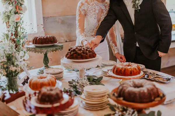 A bride and groom cutting a wedding cake at a decorated table with floral arrangements and plates.