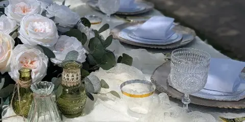 A close-up of a styled event table featuring white roses, greenery, glass vases, and elegant place settings.