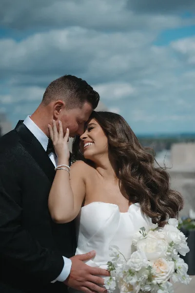 A bride and groom sharing an intimate moment outdoors, with the bride holding a bouquet of white flowers.