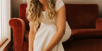 A bride with styled hair and natural makeup sitting on a red couch indoors.