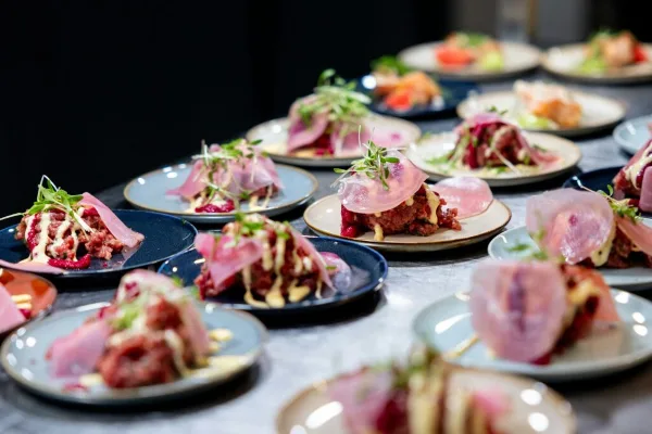 A table filled with numerous plated appetizers featuring meat, garnishes, and sauces.