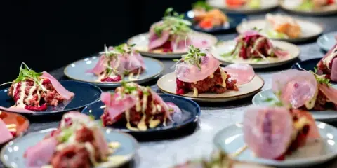 A table filled with numerous plated appetizers featuring meat, garnishes, and sauces.