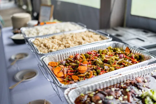 A catering buffet table with large aluminum trays filled with rice, mixed vegetables, and meat, set up for a wedding event.