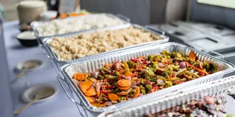 A catering buffet table with large aluminum trays filled with rice, mixed vegetables, and meat, set up for a wedding event.