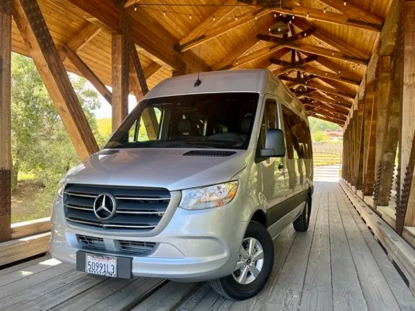 A silver Mercedes-Benz Sprinter van parked under a wooden covered bridge.