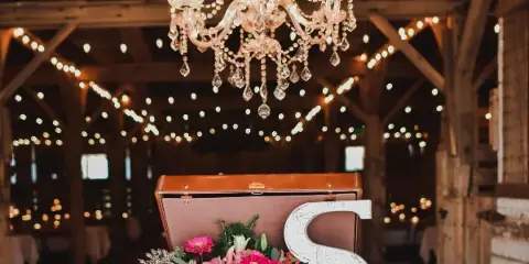 Interior view of a rustic barn wedding venue featuring a crystal chandelier, string lights, and a floral arrangement on a wooden barrel.