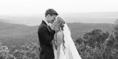A black and white photograph of a bride and groom kissing on a rocky cliff overlooking a valley.