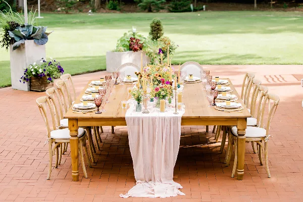 Styled outdoor wedding reception table with floral centerpiece, candles, and place settings on a brick patio.