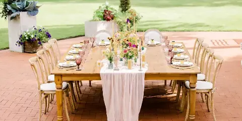 Styled outdoor wedding reception table with floral centerpiece, candles, and place settings on a brick patio.