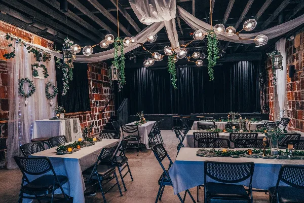 Interior of an event venue with brick walls, set up with long tables, white linens, and floral decorations for a wedding reception.