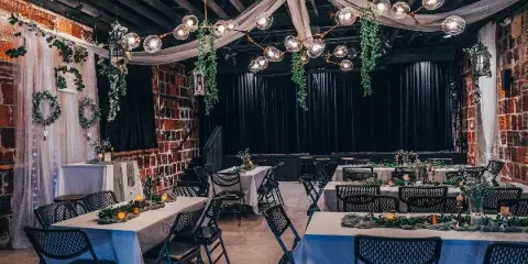 Interior of an event venue with brick walls, set up with long tables, white linens, and floral decorations for a wedding reception.