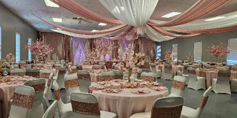 A banquet hall decorated with pink and white ceiling drapes, round tables with pink linens, and chairs with spandex covers and sequined sashes.