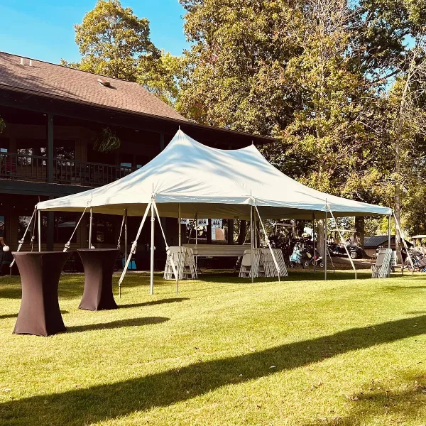 A white event tent set up on a grassy lawn with tables and chairs arranged underneath.