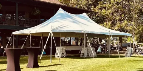 A white event tent set up on a grassy lawn with tables and chairs arranged underneath.