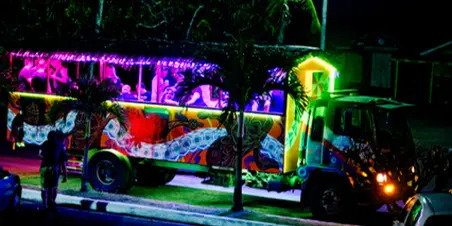 A party bus with colorful interior lighting and passengers visible through the windows at night.
