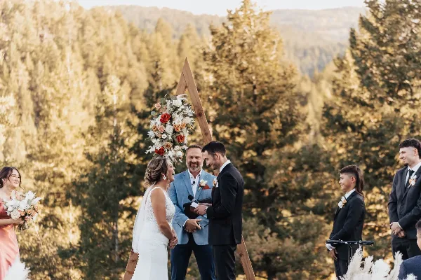 A bride and groom exchanging vows at an outdoor wedding ceremony with a floral arch and officiant.