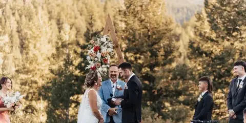 A bride and groom exchanging vows at an outdoor wedding ceremony with a floral arch and officiant.