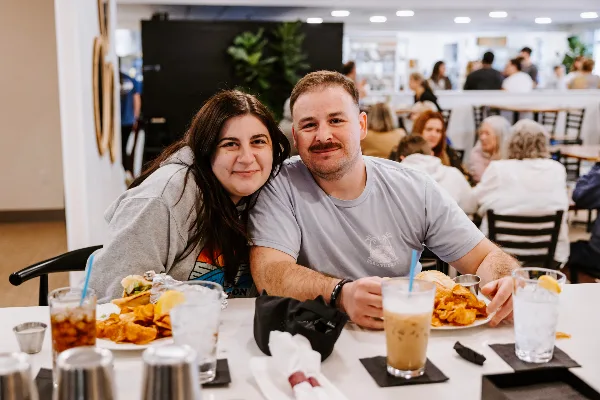 A couple seated at a table in a restaurant with plates of food and beverages.