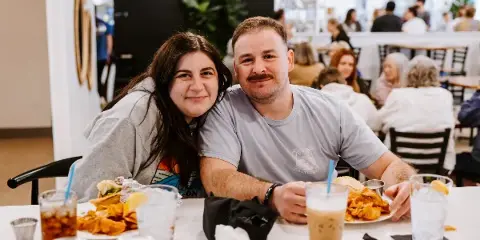 A couple seated at a table in a restaurant with plates of food and beverages.