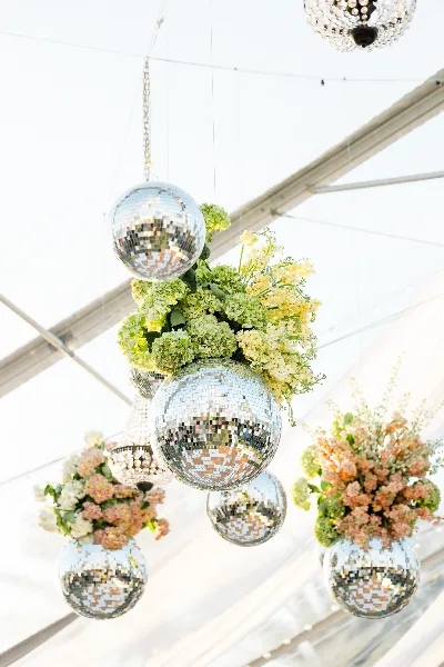 Close-up of hanging floral arrangements featuring green hydrangeas and yellow flowers intertwined with mirrored disco balls.
