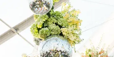 Close-up of hanging floral arrangements featuring green hydrangeas and yellow flowers intertwined with mirrored disco balls.