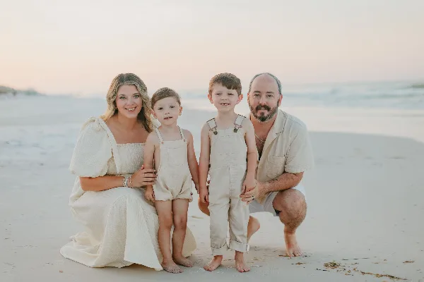 A family of four posing for a professional portrait on a sandy beach at sunset.