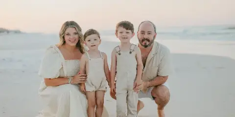 A family of four posing for a professional portrait on a sandy beach at sunset.