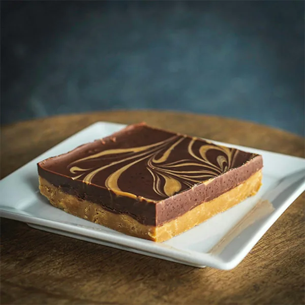 A slice of layered chocolate and caramel cake with a marbled chocolate top, served on a white square plate.