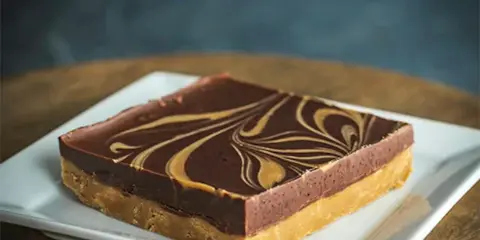 A slice of layered chocolate and caramel cake with a marbled chocolate top, served on a white square plate.
