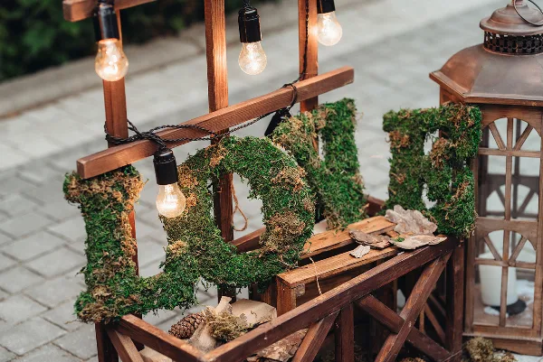 A wooden cart decorated with moss-covered letters and string lights, representing event rental decor.